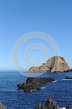 Rocky coastline of the Atlantic Ocean with waves and cliffs mountains and blue sky in Madeira Island, Portugal