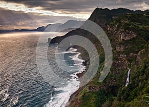 Rocky coastline of Madeira with waterfalls, wave and sunset