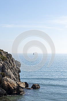 rocky coastline with a sailboat sailing with a calm sea and the horizon in the background
