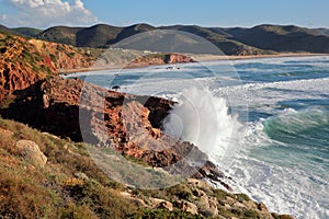 The rocky and colorful coast near Carrapateira with Amado beach in the background and strong waves, Costa Vicentina, Algarve