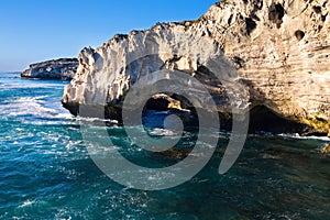 Rocky cove and ocean wave crashing into an eroded arch