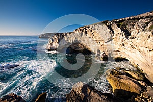 Rocky cove and ocean wave crashing into an eroded arch