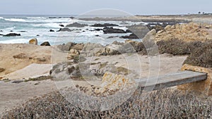 Rocky craggy ocean coast, sea waves, Monterey California. Wooden empty bench.