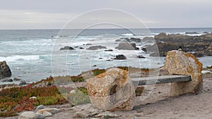 Rocky craggy ocean coast, sea waves, Monterey California. Wooden empty bench.