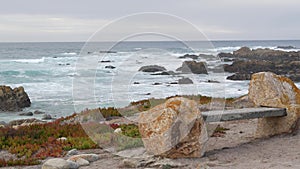 Rocky craggy ocean coast, sea waves, Monterey California. Wooden empty bench.