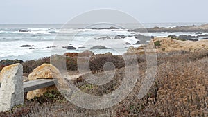 Rocky craggy ocean coast, sea waves, Monterey California. Wooden empty bench.