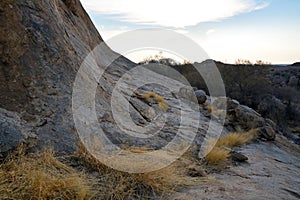 Rocky foothills of a mountain in an arid area with growing grass and boulders under a blue sky. Desert landscape and nature