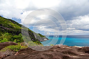 Rocky landscape in the Seychelles with sailboat in the distance