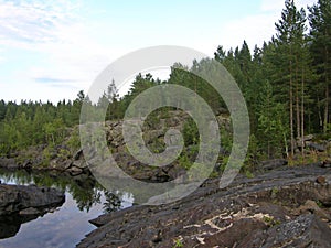 A rocky landscape with trees and rocks in the foreground. Suna River, Poor Porog Waterfall, Girvas