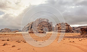 Rocky massifs on red orange sand desert, overcast sky in background - typical scenery in Wadi Rum, Jordan