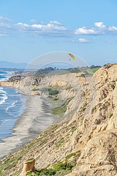 Rocky mountain bordering the shoreline of ocean aith parachuters and blue sky