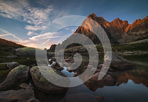 Rocky Mountain Peak and Mountain Lake with Rocks in Foreground at Sunrise