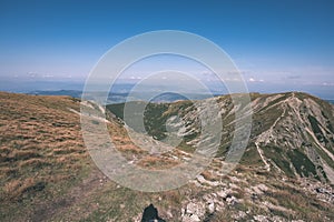 Rocky mountain tops with hiking trails in autumn in Slovakian Tatra western Carpathian with blue sky and late grass on hills.