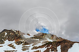 Rocky mountains covered with snow drifts, a cable car with gondolas and people