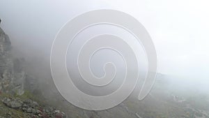 Rocky mountainside in fog. Shot. Top view of rock falls on mountainside. Dense fog envelops rock in autumn cloudy day