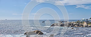 Rocky ocean coast on sunny summer day with blue skies and clear blue water, outside in nature. Serene and calm sea