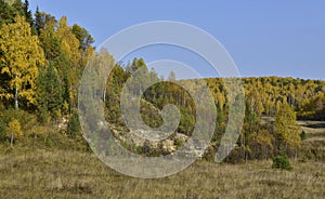 A rocky outcrop of a steep slope of a dry ravine overgrown with an autumn forest. In the foothills of the Western Urals, golden au