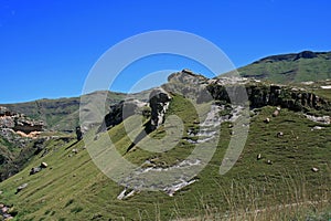 ROCKY OUTCROPS ABOVE GREEN SLOPES IN THE DRAKENSBERG MOUNTAIN RANGE