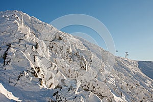 The rocky peak of mountain Snezka. Winter, morning time, chairlift connecting peak Snezka with town Pec pod Snezkou , krkonose