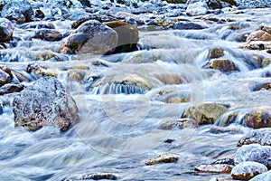 Rocky riffle on a clear mountain river close-up, the water is blurred in motion