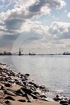 Rocky river bank landscape with a shipping port in the distance. the sun\'s rays flash in the water
