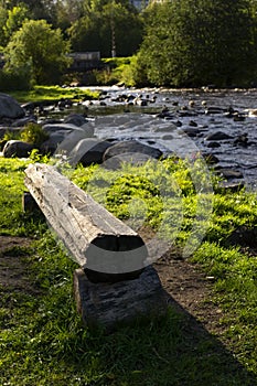 Rocky river in city park in autumn with a log bench, vertical