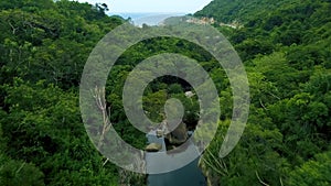 Rocky river in green forest and winding road in mountain aerial landscape. View from above flying drone over stony river