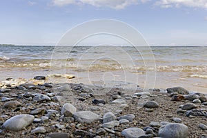 rocky sand beach with blue cold baltic sea and blue sky