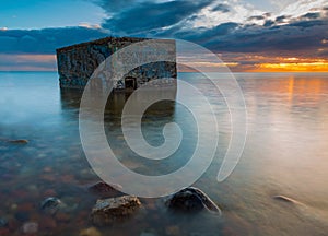 Rocky sea shore with old bunker in sea, long exposure photo