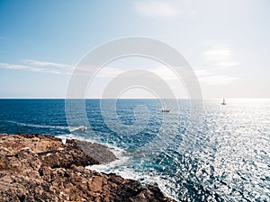 Rocky seashore. Sailboats sail in the distance under the bright sun