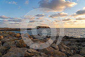 Rocky shore of Agios Georgios Cyprus. View of the island Yeronisos. Sunset at Agios Georgios Pegeias harbor in Paphos