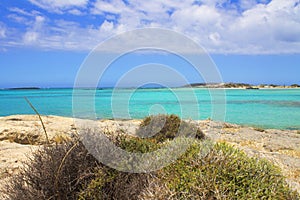 Rocky shore with bashes, turkuoise sea and clouds in blue sky.