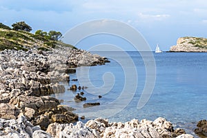 The rocky shore of the island of Lavsa, Croatia, and the yacht going to the sea photo
