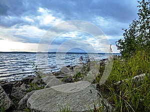 Rocky shore of lake Uvildy in inclement weather, sky with gray clouds