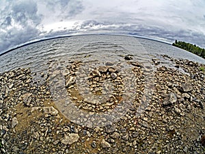 Rocky shore of lake Uvildy in inclement weather, sky with gray clouds, fishay lens photo
