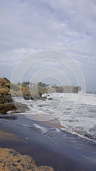 Rocky shore of muttom beach with sea waves in yellow and black sand