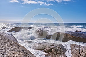 A rocky shore and a view of the ocean with waves, blue sky copy space, and a horizon in the background in Camps Bay