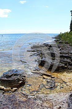 The rocky shoreline of Lake Michigan with people swimming in the distance at Cave Point County Park in Wisconsin