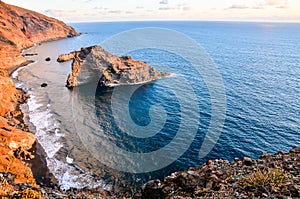A rocky shoreline with a large rock in the middle of the ocean