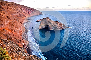 A rocky shoreline with a large rock in the middle of the ocean