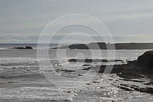 a rocky shoreline with waves crashing under a partly cloudy sky, embodying nature's serene yet untamed beauty