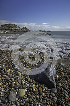 A rocky shoreline, with a white lighthouse on a headland. The beach is Bracelet Bay, Mumbles, south Wales