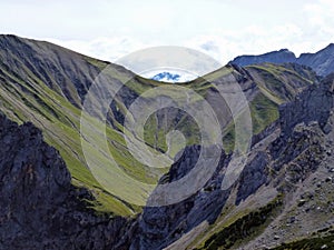 The rocky slopes of the mountains are overgrown with green grass under a cloudy sky. Beautiful mountain landscape with blue sky