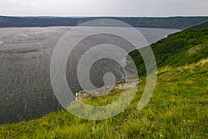 Rocky steep forested and grassy shore of the river bay in cloudy weather. Panoramic view of the river in summer in cloudy weather