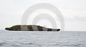 Rocky uninhabited island plateau cliff in ocean with clouds, sky & horizon in background