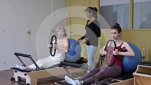 rofessional hispanic female trainer controlling young woman exercising wunda chair with pilates ring to strengthen