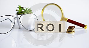 ROI concept on the wooden cubes and flower ,glasses ,coins and magnifier on white background