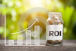 ROI Return on Investment Word With Coin In Glass Jar and graph