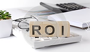 ROI written on a wooden cube on keyboard with office tools