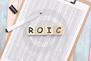 ROIC - inscription on wooden cubes on a white background along with a tabular document. finance and business concept